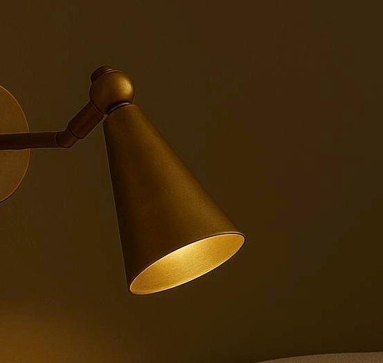 Brass cone sconce lit, warm glow from inside the shade