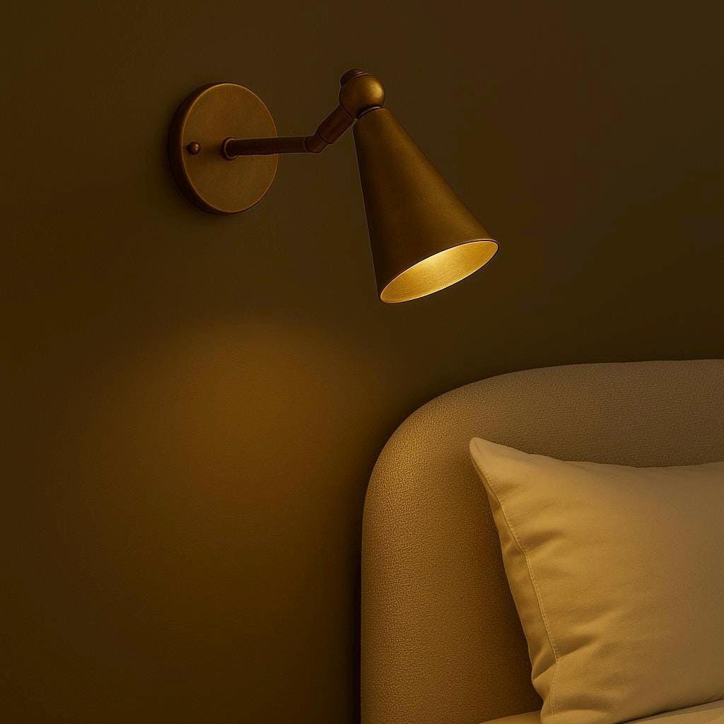 Brass cone wall sconce with adjustable arm, lit above a bed